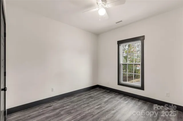 an empty room with wooden floor chandelier fan and windows