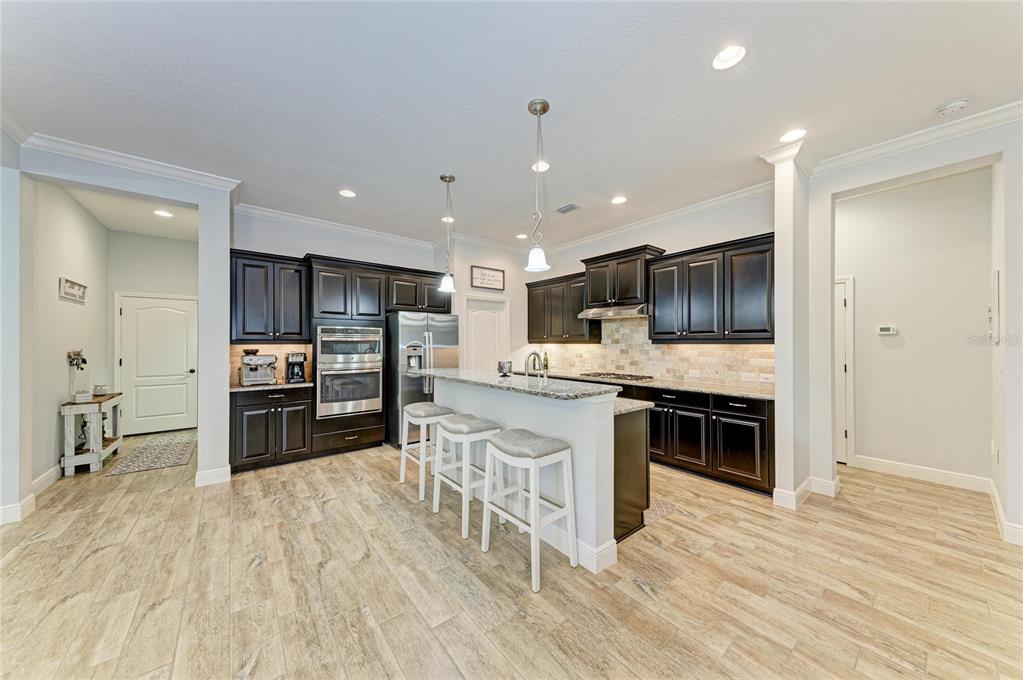 12642 Harney Street Venice, FL 34293 - Photo 12 of 85 a kitchen with stainless steel appliances kitchen island granite countertop a stove top oven a sink dishwasher a refrigerator and a dining table with wooden floor