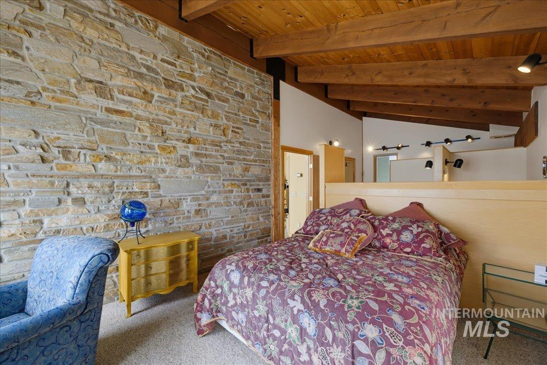 3800 Warren Wagon Road McCall, ID 83638 - Photo 20 of 50 Natural stone accent wall with exposed wood ceiling beams, track lighting, and a light wood headboard