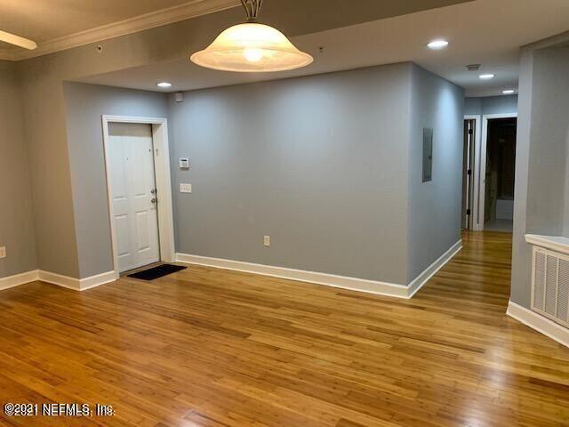 an empty room with wooden floor and way to kitchen