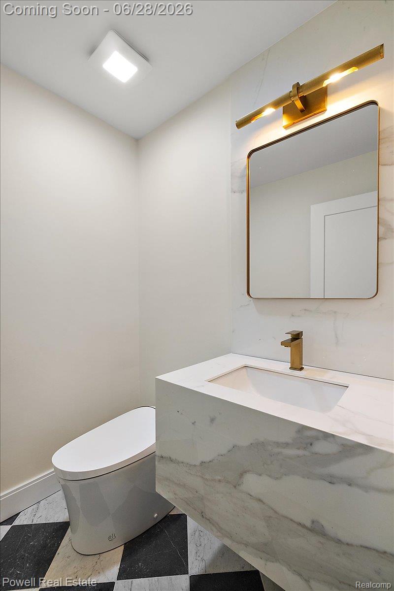 1447 Ravineview Court, Unit C12 Bloomfield Hills, MI 48304 - Photo 12 of 49 Modern bathroom featuring a floating vanity with an integrated sink, a sleek gold-tone faucet, a rectangular mirror with a gold-tone frame, and a complementary gold-tone light fixture