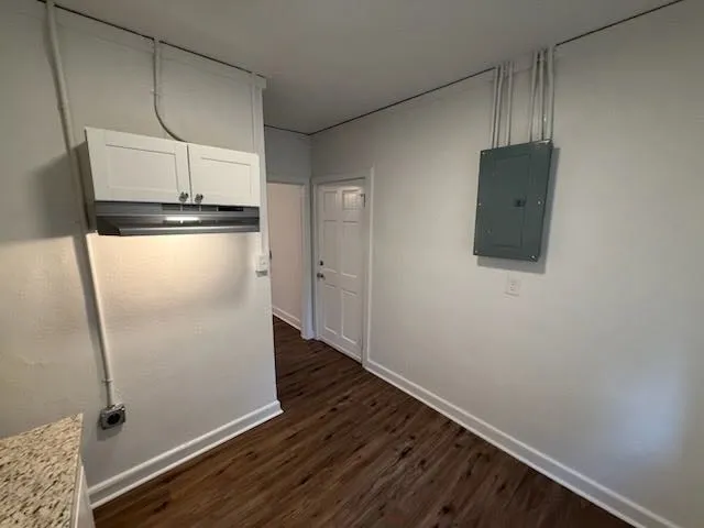 a view of a refrigerator in kitchen and an empty room with wooden floor