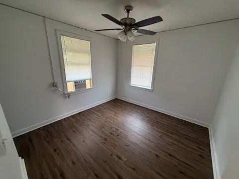 an empty room with wooden floor fan and windows
