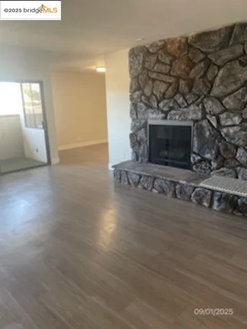 an empty room with wooden floor fireplace and windows