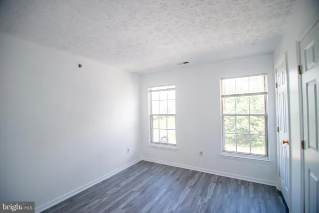 a view of an empty room with wooden floor and window