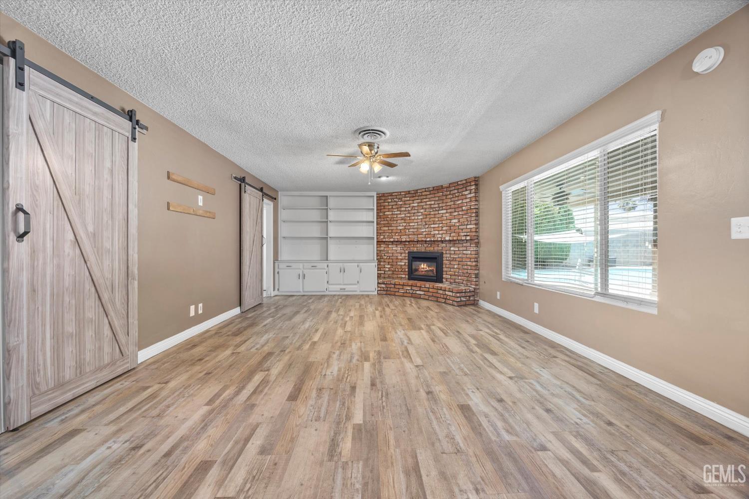 Undisclosed Address Bakersfield, CA 93308 - Photo 22 of 50 an empty room with windows a fireplace and wooden floor