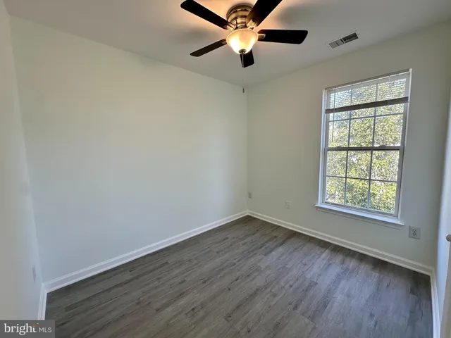 an empty room with wooden floor ceiling fan and windows