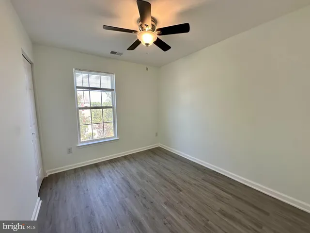 an empty room with wooden floor fan and windows