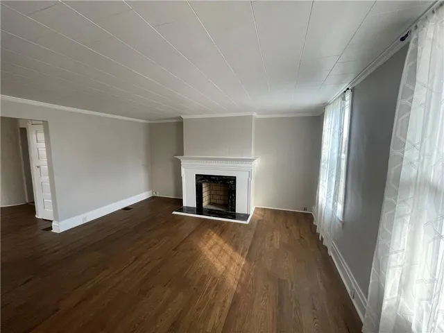 a view of an empty room with wooden floor fireplace and a window