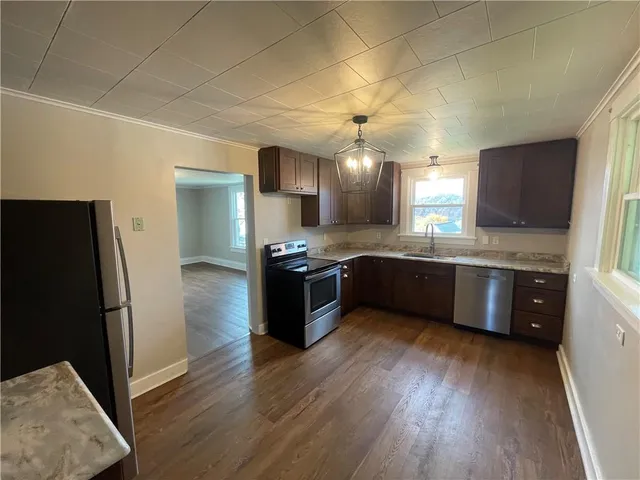 a kitchen with stainless steel appliances kitchen island granite countertop a refrigerator a sink dishwasher a stove and white countertops with wooden floor