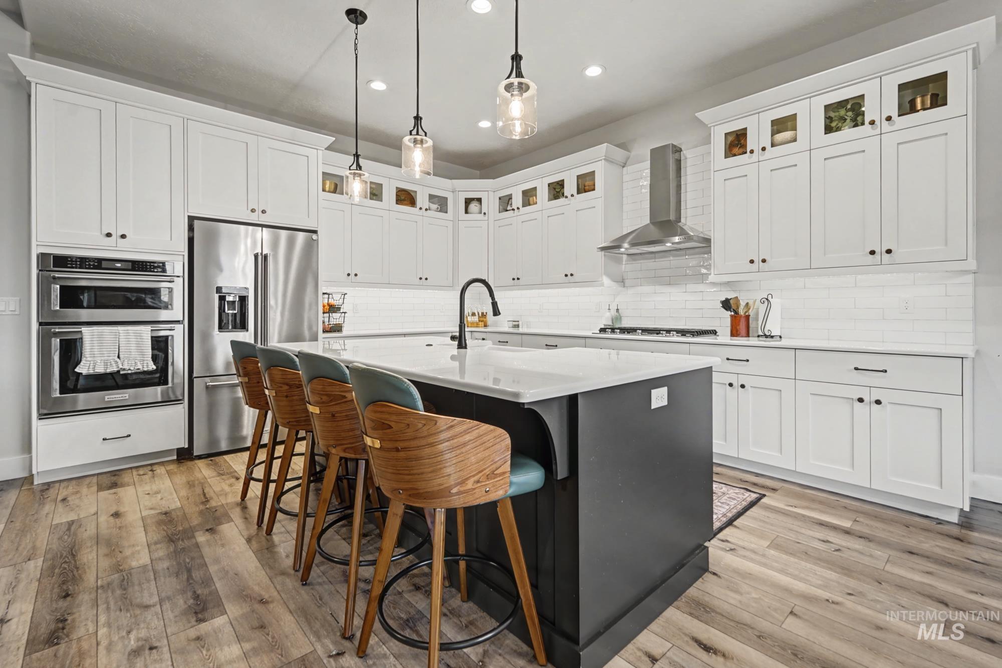 18357 North Burnt Car Way Boise, ID 83714 - Photo 4 of 48 Kitchen featuring stainless steel appliances, glass insert cabinets, decorative light fixtures, a center island with sink, and two tone cabinetry