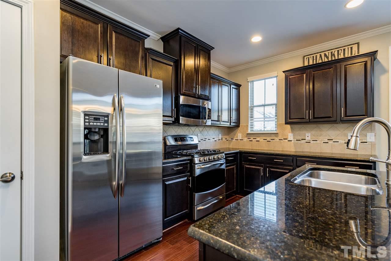 1521 Rodessa Run Raleigh, NC 27607 - Photo 16 of 29 Kitchen features easy island/bar for eating/cooking/hanging out. Granite counters, stainless appliances, full pantry with wooden shelving, ceramic tile backsplash and the loved dark cabinets.