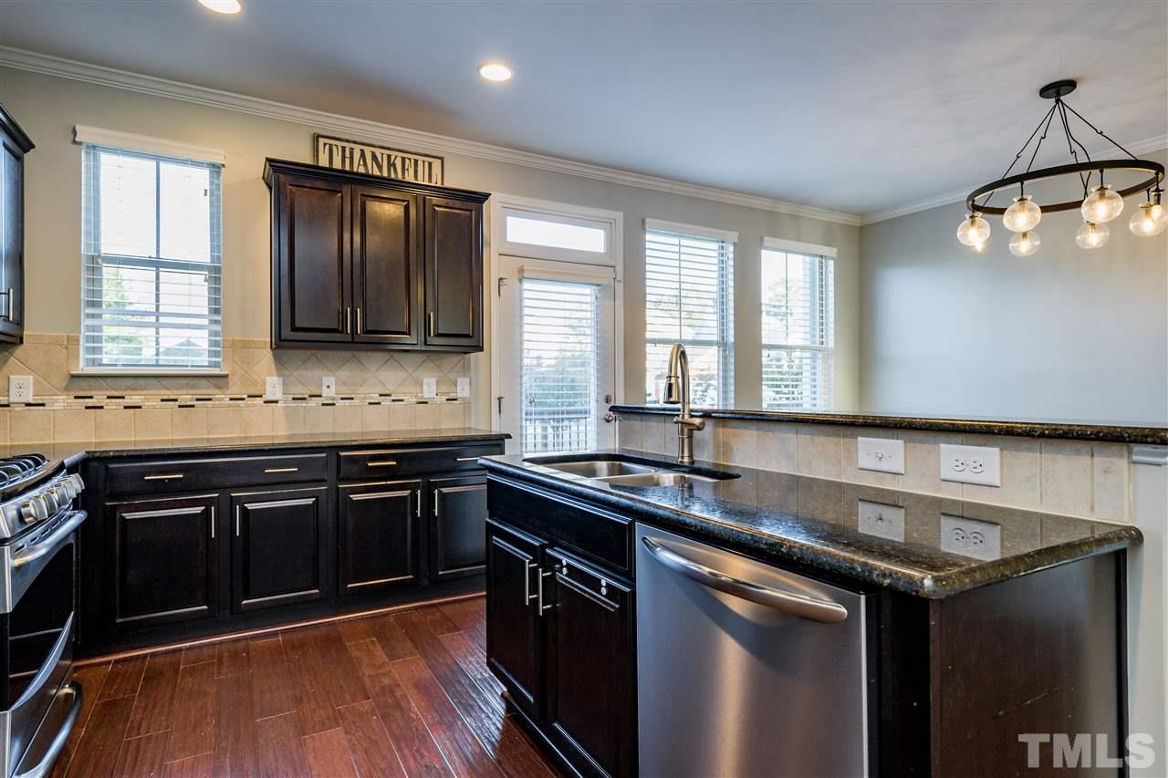 1521 Rodessa Run Raleigh, NC 27607 - Photo 17 of 29 Kitchen features easy island/bar for eating/cooking/hanging out. Granite counters, stainless appliances, full pantry with wooden shelving, ceramic tile backsplash and the loved dark cabinets.