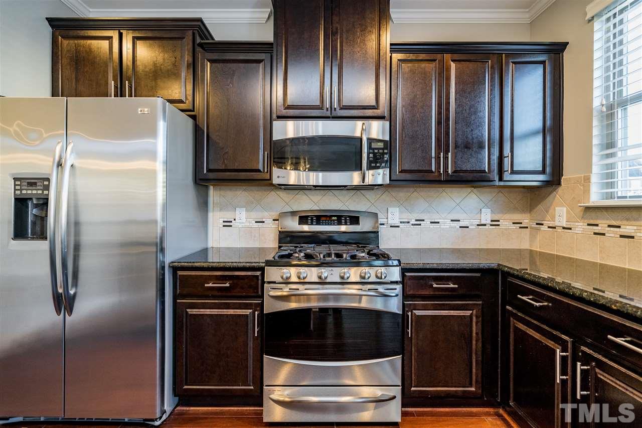 1521 Rodessa Run Raleigh, NC 27607 - Photo 18 of 29 Kitchen features easy island/bar for eating/cooking/hanging out. Granite counters, stainless appliances, full pantry with wooden shelving, ceramic tile backsplash and the loved dark cabinets.