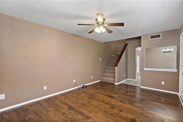 a view of an empty room with wooden floor and a ceiling fan