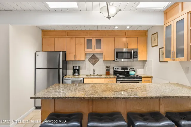 a kitchen with stainless steel appliances granite countertop a refrigerator a stove a sink a dining table and chairs with wooden floor