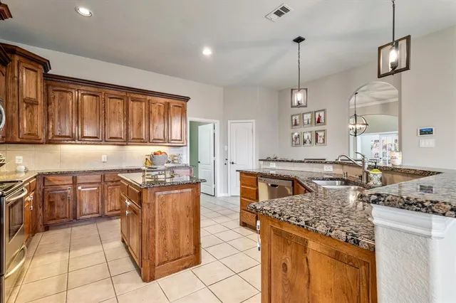 a kitchen with stainless steel appliances granite countertop a stove a sink dishwasher and a refrigerator with wooden cabinets