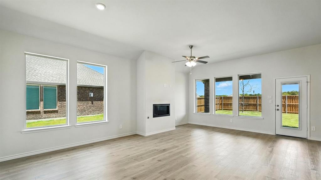 4191 Waldron Trail Forney, TX 75126 - Photo 8 of 20 Spacious living area featuring light wood-finish flooring, a contemporary fireplace, and multiple large windows