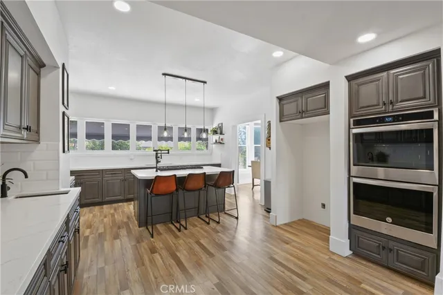 a kitchen with stainless steel appliances kitchen island granite countertop a refrigerator a stove top oven and a dining table with wooden floor