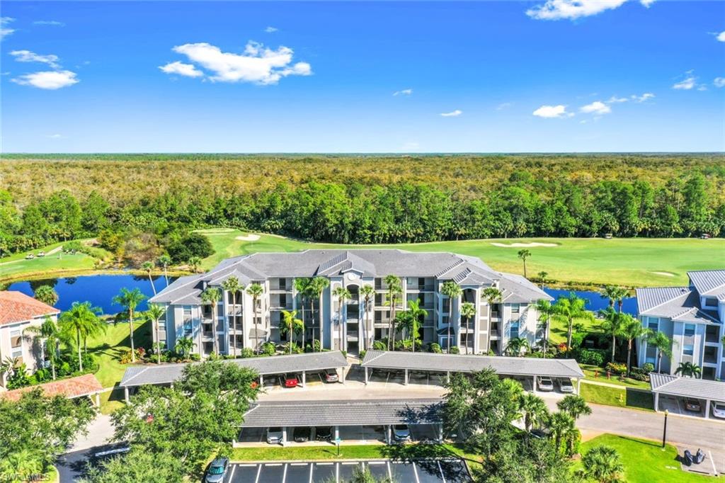 10329 Heritage Bay Boulevard, Unit 1641 Naples, FL 34120 - Photo 1 of 22 Drone / aerial view of a local golf course, a heavily wooded area, a nearby body of water, and apartment complex / building