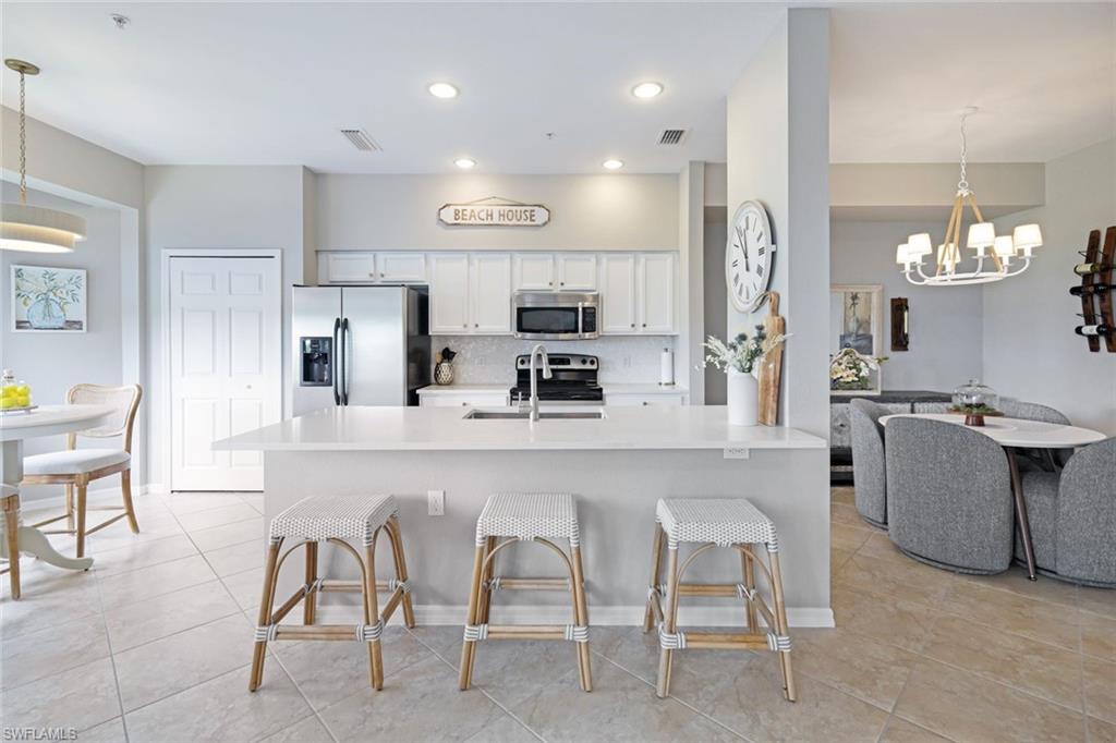 10329 Heritage Bay Boulevard, Unit 1641 Naples, FL 34120 - Photo 11 of 22 Kitchen featuring appliances with stainless steel finishes, a chandelier, a breakfast bar, tasteful backsplash, and light tile patterned floors