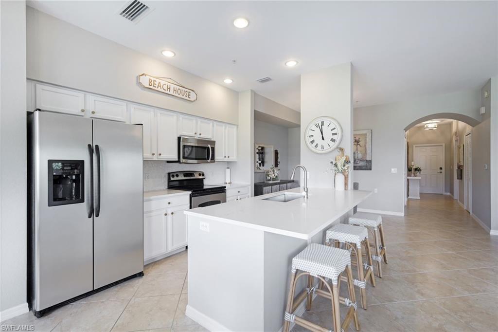 10329 Heritage Bay Boulevard, Unit 1641 Naples, FL 34120 - Photo 7 of 22 Kitchen with appliances with stainless steel finishes, a sink, arched walkways, white cabinetry, and light tile patterned floors