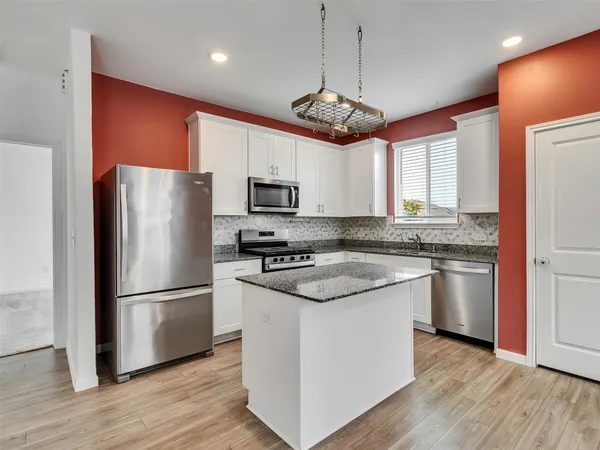 a kitchen with stainless steel appliances granite countertop a refrigerator a stove a sink dishwasher a refrigerator and a dining table with wooden floor