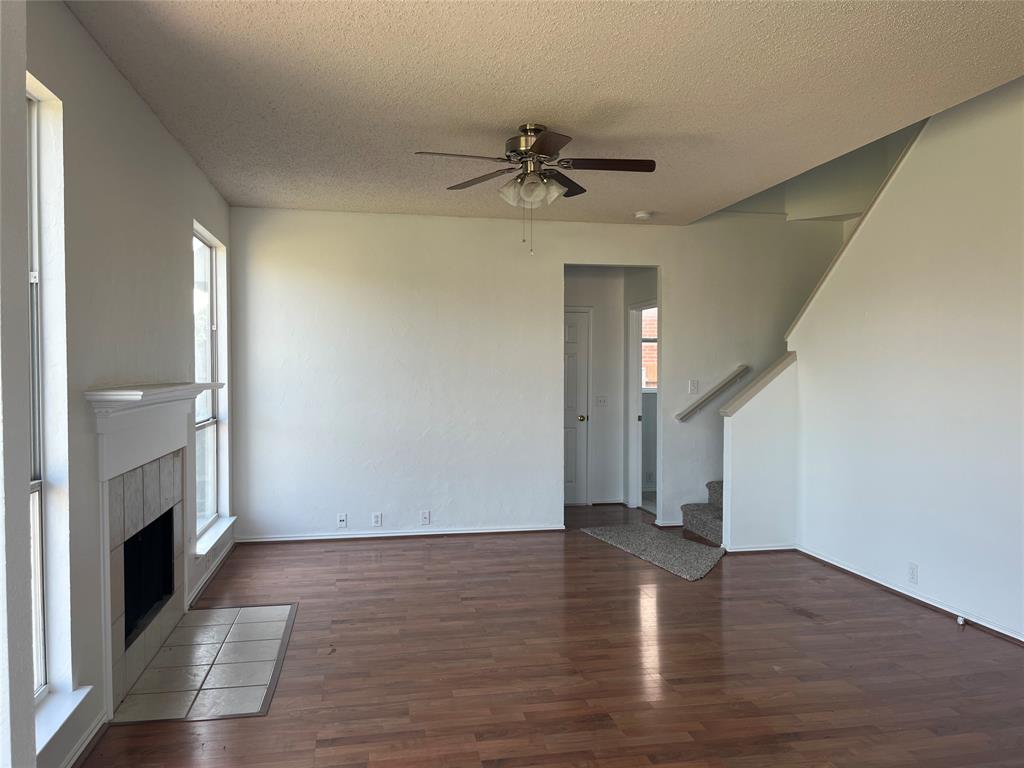 7929 Park Ridge Drive Fort Worth, TX 76137 - Photo 4 of 13 Spacious interior featuring wood-finish flooring, a ceiling fan, and a fireplace with a white mantel and tile hearth