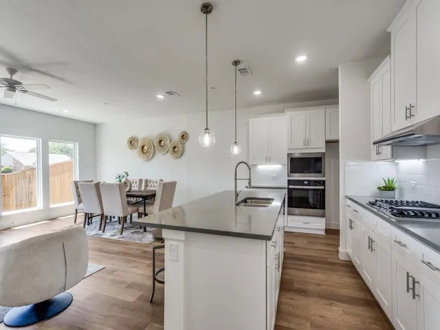 a kitchen with stainless steel appliances kitchen island granite countertop a stove a sink a oven a dining table and chairs with wooden floor