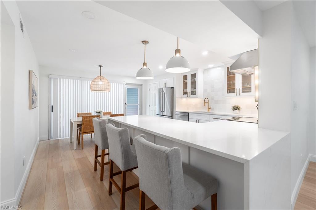 1222 Gordon Drive, Unit 2 Naples, FL 34102 - Photo 8 of 24 Kitchen with glass insert cabinets, a kitchen breakfast bar, a peninsula, pendant lighting, and light wood-type flooring