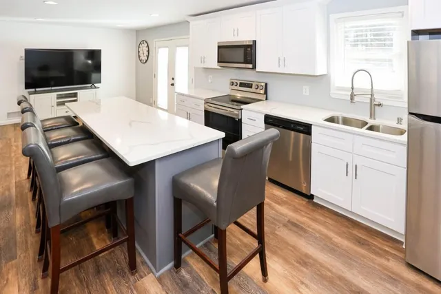 a living room with stainless steel appliances furniture a flat screen tv and kitchen view