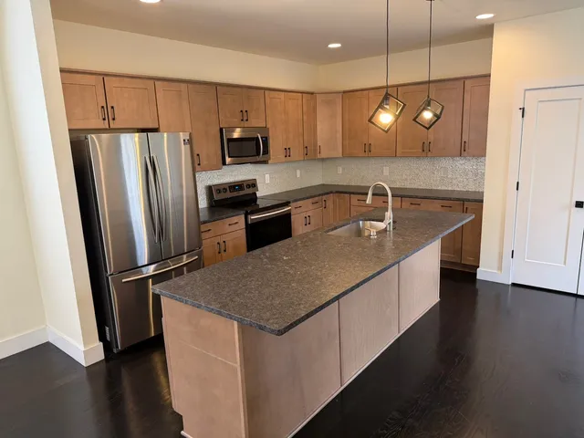 a kitchen with stainless steel appliances granite countertop a refrigerator a sink dishwasher a stove and a refrigerator with wooden floor