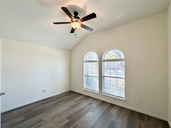 an empty room with wooden floor fan and windows