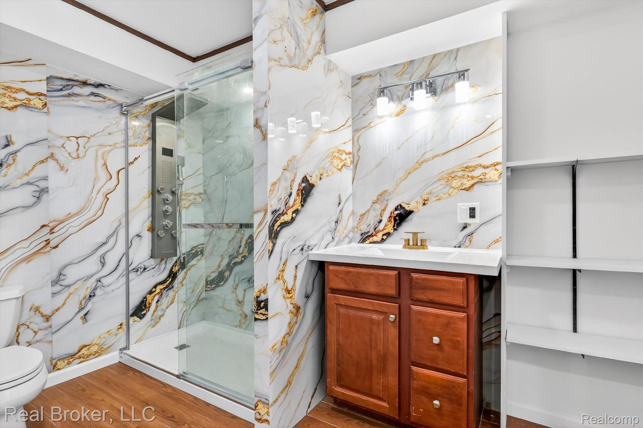 48050 Hull Road Belleville, MI 48111 - Photo 21 of 39 Bathroom featuring floor-to-ceiling marbled wall tiling, a glass-enclosed shower with a multi-function panel, wood-finish flooring, a vanity with wood cabinetry and a white countertop, and built-in shelving