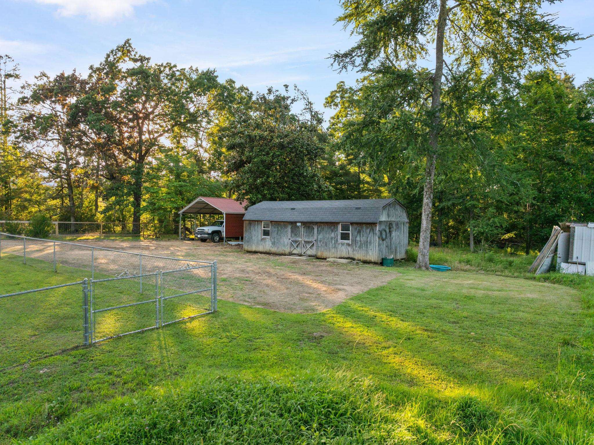 66 County Road 511 Corinth, MS 38834 - Photo 34 of 40 Spacious outdoor area featuring a wood-sided outbuilding with a shingled roof, a red metal carport, and a chain-link fence enclosing a portion of the property