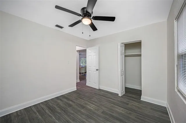 an empty room with wooden floor ceiling fan and windows
