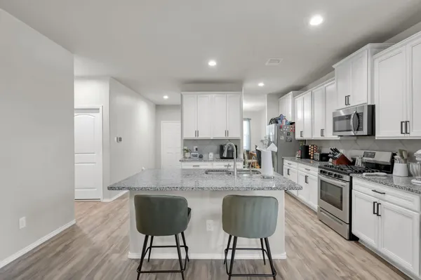 a kitchen with stainless steel appliances granite countertop a stove top oven a sink dishwasher and a refrigerator with wooden floor