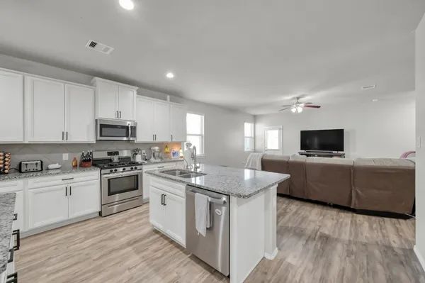 a kitchen with stainless steel appliances granite countertop a stove top oven a sink a refrigerator and white cabinets with wooden floor