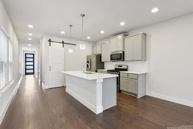 a kitchen with stainless steel appliances kitchen island granite countertop a stove top oven a sink a refrigerator and white cabinets with wooden floor