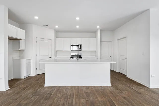 a large white kitchen with kitchen island a sink wooden floor and stainless steel appliances