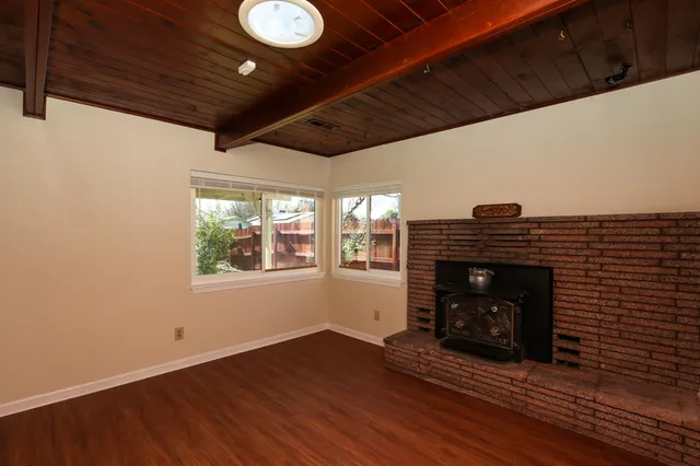 a view of an empty room with wooden floor fireplace and a window