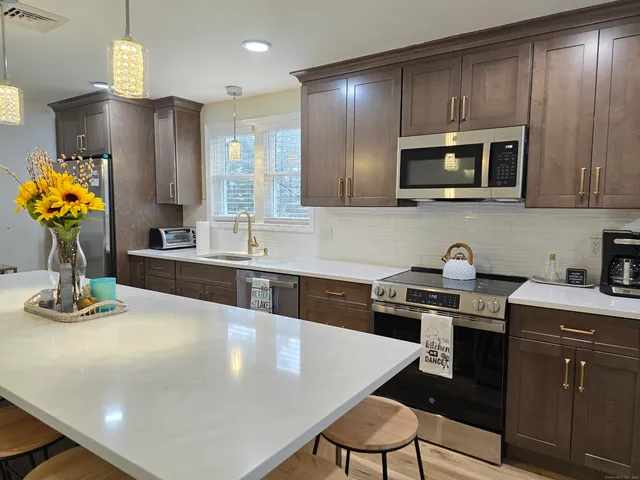 a kitchen with stainless steel appliances a stove a sink a microwave a refrigerator white cabinets and wooden cabinets