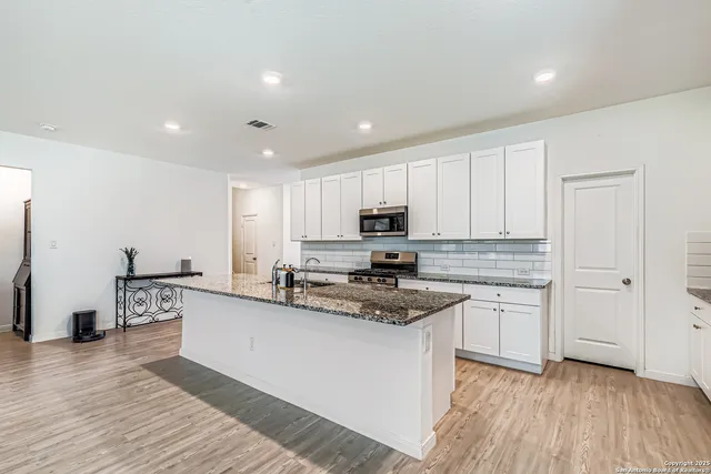 a kitchen with stainless steel appliances granite countertop a sink dishwasher a refrigerator and white cabinets with wooden floor