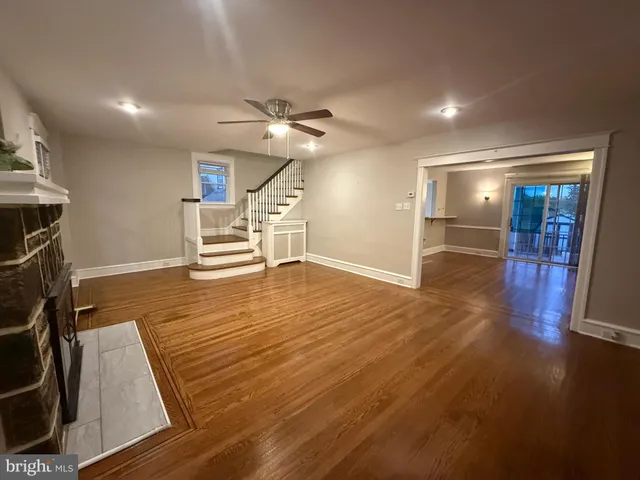 a view of an empty room with wooden floor a ceiling fan and windows