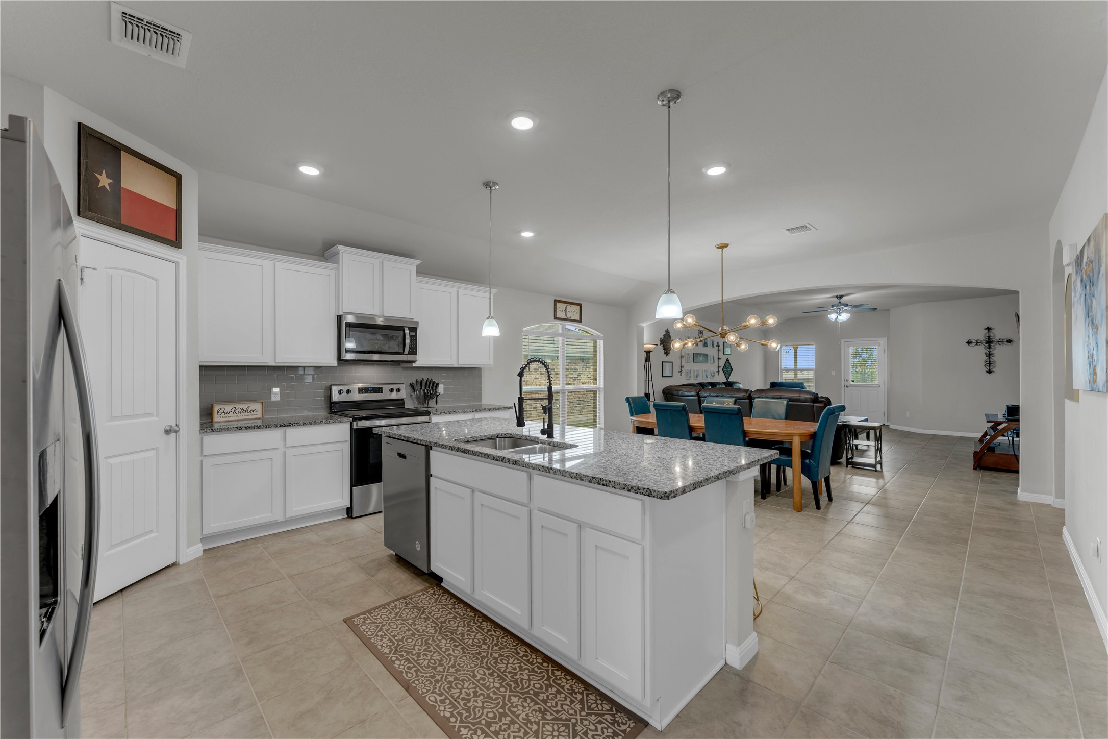 132 Cinnamon Loop Burnet, TX 78611 - Photo 4 of 27 Modern kitchen featuring an island with a sink, white cabinetry, stainless steel appliances, a gray tile backsplash, and light-toned tile flooring