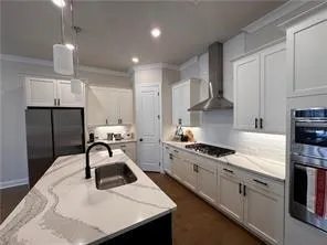 a kitchen with stainless steel appliances kitchen island granite countertop a refrigerator a sink a stove and white cabinets with wooden floor