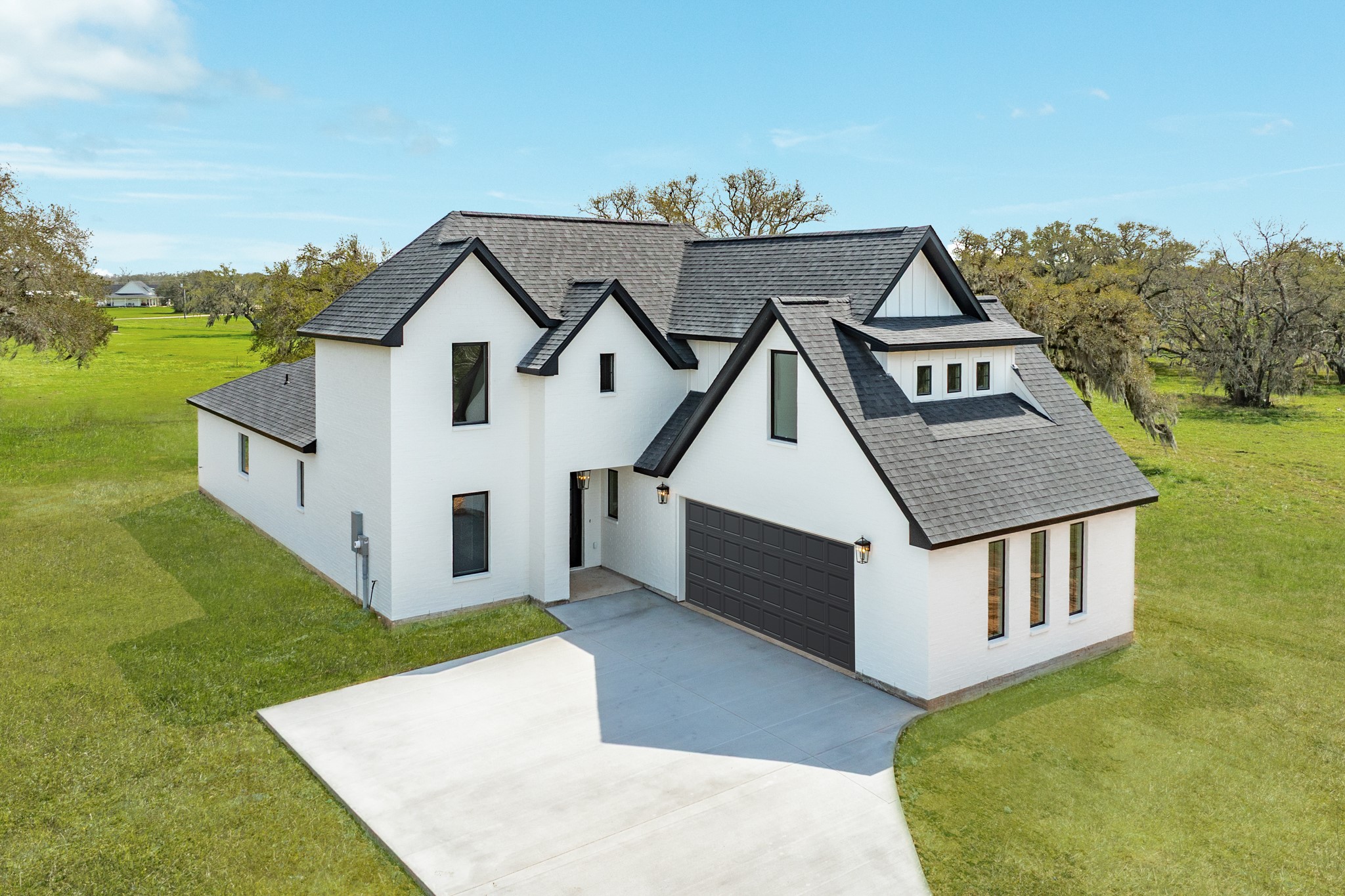 This photo showcases a modern, two-story home with a clean white exterior and dark roof. It features a spacious driveway leading to a double over sized garage, surrounded by mature trees, offering a serene and private setting.