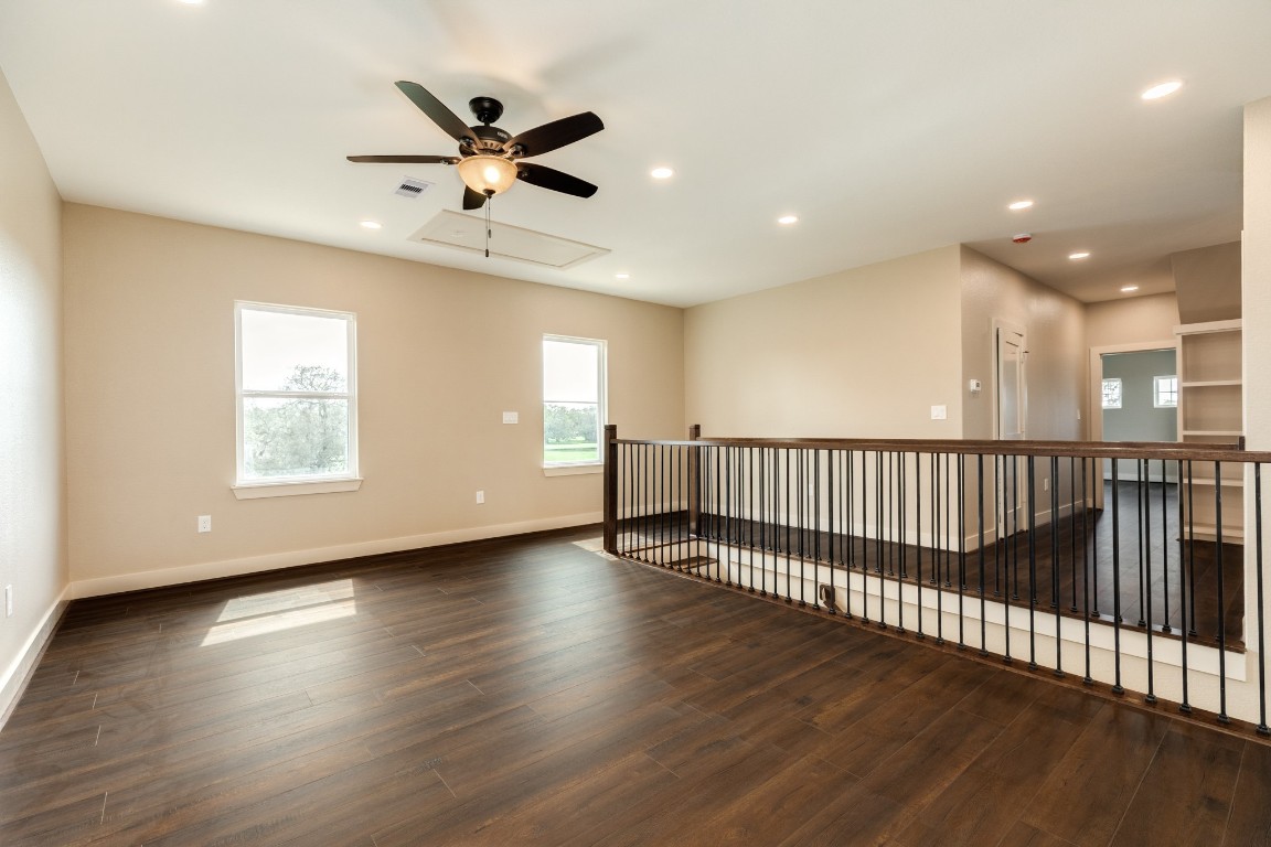 1737 Flintlock Court Angleton, TX 77515 - Photo 34 of 47 This spacious, open area features rich wood flooring, neutral walls, and ample natural light. It includes a ceiling fan, recessed lighting, and a modern railing overlooking a lower level, creating an inviting and versatile space.