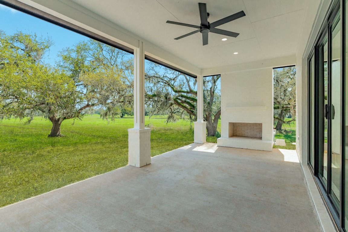 1737 Flintlock Court Angleton, TX 77515 - Photo 5 of 47 This photo showcases a spacious covered patio with a ceiling fan and fireplace, offering a serene view of lush greenery and mature trees, ideal for outdoor relaxation.