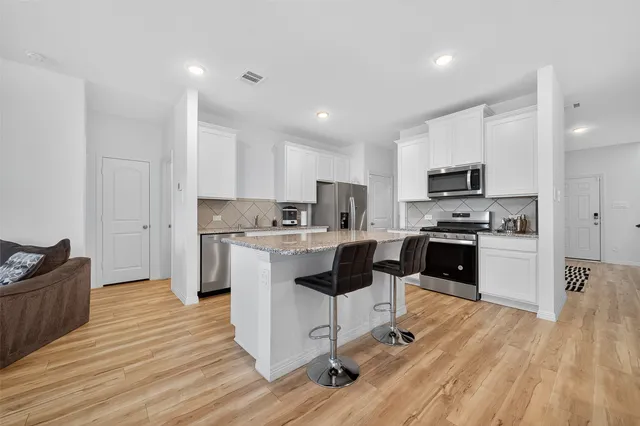 a kitchen with granite countertop a refrigerator oven a sink dishwasher and white cabinets with wooden floor